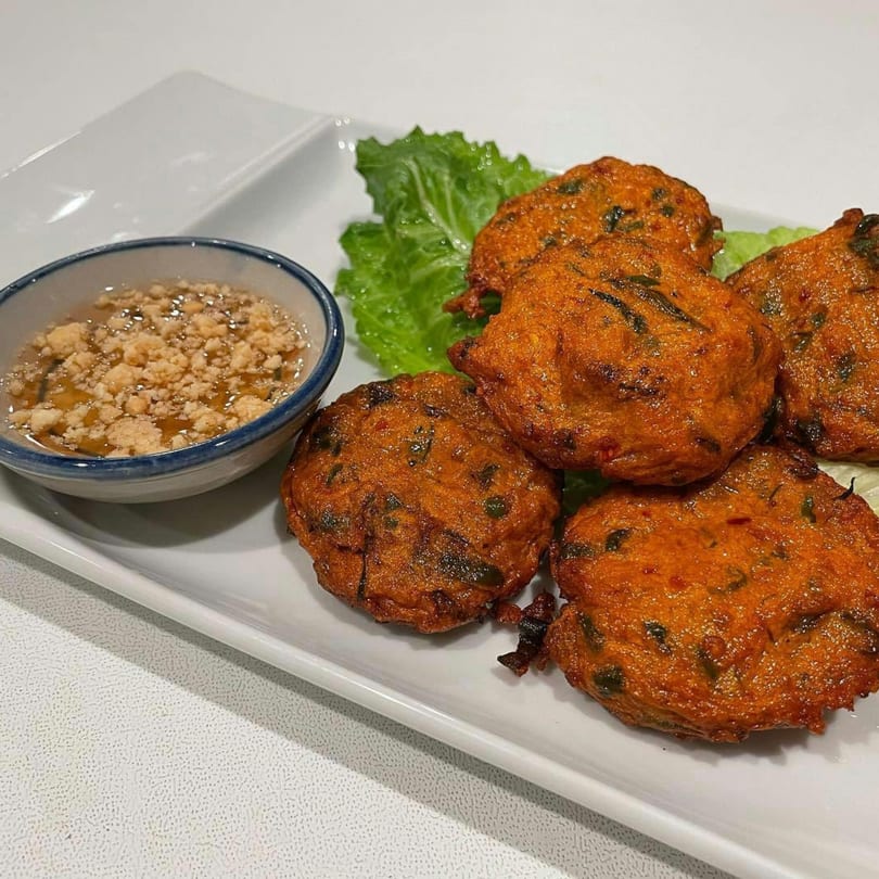 Golden-brown Thai fish cakes with green herbs, served with a sweet and savory dipping sauce.